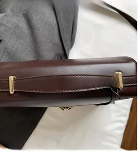 Detail of a dark brown leather handbag featuring a sturdy top handle and gold metal hardware