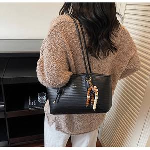Close-up of black woven leather tote bag with wooden bead tassel and gold logo detail