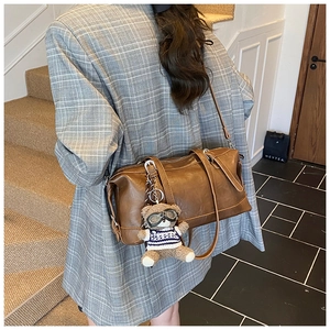 Dettaglio borsa Boston marrone vintage con ciondolo a orsetto su modella in blazer grigio