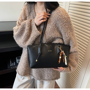 Detail of black woven texture shoulder bag with ethnic beaded charm and gold logo