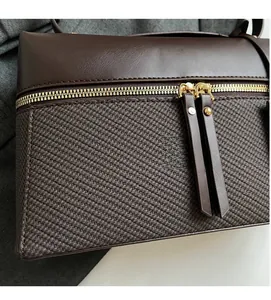 Detail of dual gold zippers and texture on a brown leather and twill fabric handbag