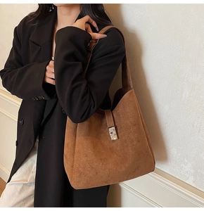 Detail of caramel suede hobo bucket bag with silver buckle worn by a model in a suit