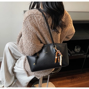 Detail of black woven tote bag with ethnic tassel charm and leather straps worn by model