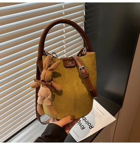 Close-up of mustard green suede bucket bag with leather handle and cute rabbit pendant