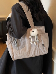 Large taupe nylon tote bag with plush monster charm and side pockets shown on shoulder