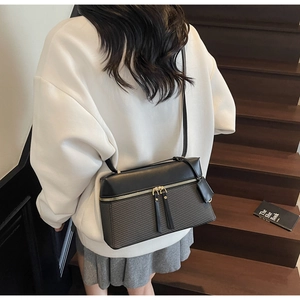 Detail of a minimalist black and grey crossbody camera bag featuring leather tassels and strap