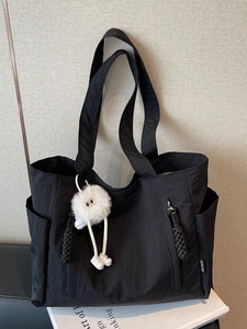 Large black nylon tote bag with front zipper and plush charm on a black chair