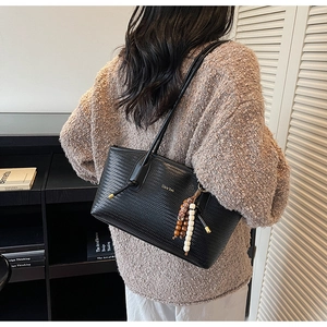 Detail of black woven shoulder bag with boho charm and slim leather strap for women