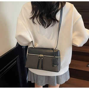 Detail of a black and grey paneled crossbody bag with golden dual zippers on a model