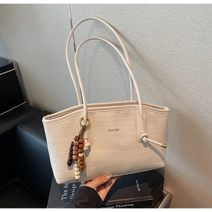 Detail of cream woven tote bag with Chrs'2ab logo and decorative wooden bead charm