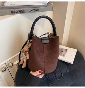 Detail of brown suede bucket bag featuring black handle, DM logo and bunny pendant