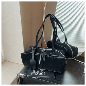 Detail of a black suede cylindrical pillow bag with silver dual zippers and a shoulder strap