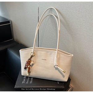 Detail of woven texture cream tote bag with wooden bead charm on a black book