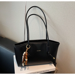 Detail of black woven texture tote bag featuring golden logo and wooden bead pendant
