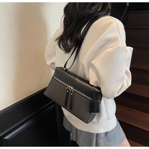 Detail of a minimalist black and grey patchwork shoulder bag shown on a female model