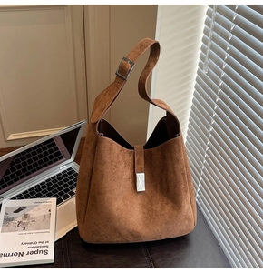 Detail of a brown suede hobo bag with a silver square buckle in a modern office setting