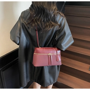 Detail of dark red crossbody bag with woven texture on a black leather jacket