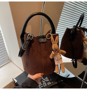 Detail of dark brown matte bucket bag with black leather handle and cute rabbit pendant