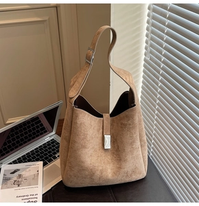 Detailed close-up of a brown suede bucket bag with silver buckle and wide shoulder strap