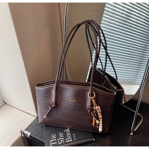 Detail of dark brown woven tote bag with gold logo and decorative beaded tassel charm