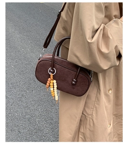 Dettaglio di una borsa Boston in camoscio marrone scuro con ciondolo di perline su un cappotto