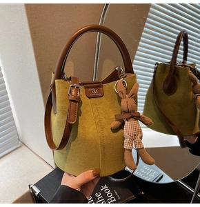 Detail view of green suede bucket bag with leather handles and cute knit rabbit charm