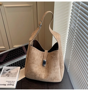 Detail of light brown suede hobo bag with metal buckle on a desk with a laptop