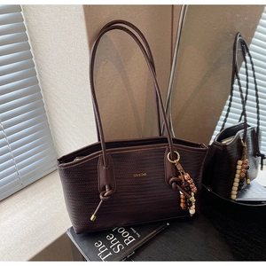 Close-up of a woven dark brown tote bag with beaded charm and gold logo detail