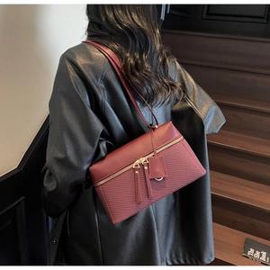 Detail of burgundy rectangular shoulder bag featuring dual gold zippers and paneled texture