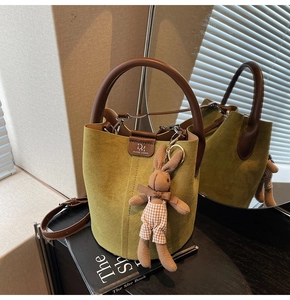Detail of green suede bucket bag with leather handles and cute rabbit plush charm
