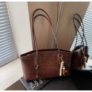 Close-up of brown woven texture tote bag with leather straps and beaded pendant