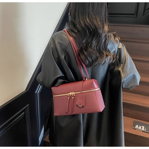 Detail of dark red leather shoulder bag with woven texture and gold dual zipper