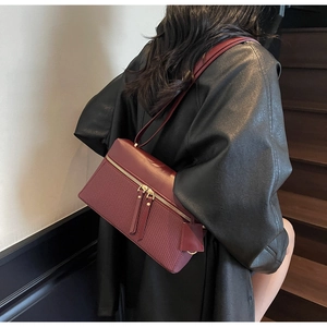 Detail of burgundy shoulder bag with textured weaving and double zippers on a leather jacket