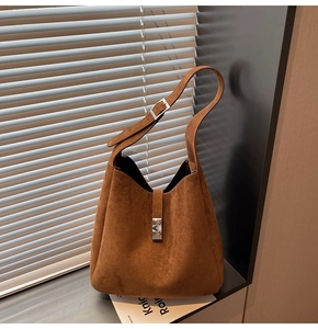 Detailed view of brown matte bucket bag with metal buckle under soft window light shadows