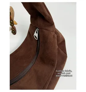 Détail du sac croissant en daim marron foncé avec tissu résistant et breloque en bois