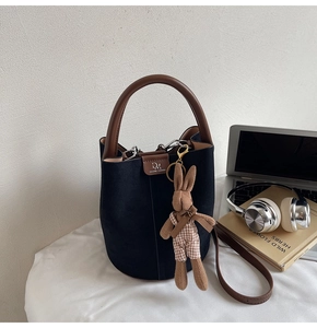 Detail of black matte bucket bag featuring a brown leather handle and cute rabbit charm