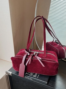 Chic burgundy suede pillow bag with dual straps and zippers in a minimalist setting