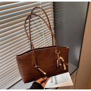 Detail of woven brown tote bag featuring metallic logo and vintage beaded tassel charm