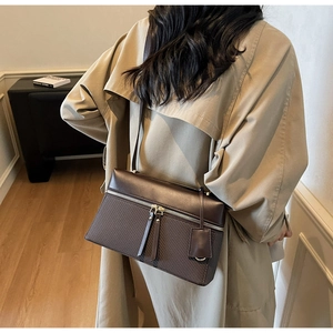 Detail of a brown structured shoulder bag featuring leather and woven texture mix on a model