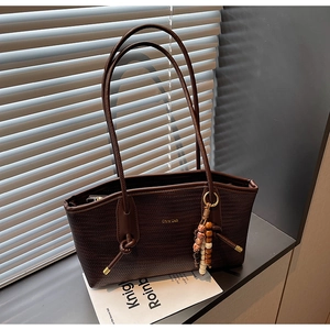 Detail of dark brown woven leather tote bag with wooden bead tassel and shoulder strap
