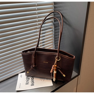 Detail of dark brown woven tote bag with beaded tassel charm and golden logo