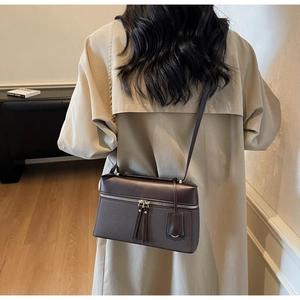 Detail of dark brown crossbody bag with woven texture and gold dual zippers on a model