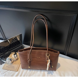 Detail of dark brown woven tote bag with slim shoulder straps and decorative bead tassel