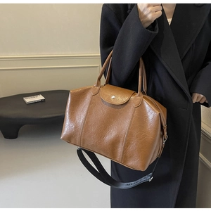 Close-up of brown polished leather Boston bag with decorative flap and metal buckle detail