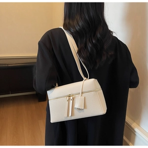 Close-up of cream square shoulder bag with woven texture worn by model in black coat