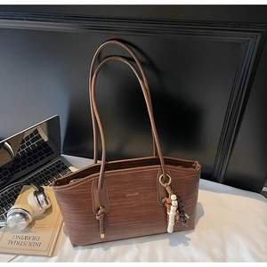 Detail of dark brown tote bag with woven texture and bead charm in an office setting