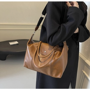 Model wearing a large brown tote bag with glossy wrinkled texture and wide strap