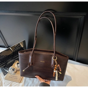Close-up of deep brown woven leather tote bag with gold logo and beaded strap charm
