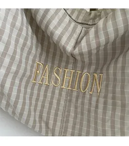 Close-up of gold FASHION embroidery on a beige plaid fabric shoulder bag texture