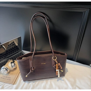 Detail of dark brown woven tote bag with beads, laptop, and office lifestyle items